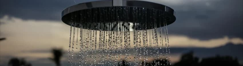 Water falling from a round rain shower head at dusk.