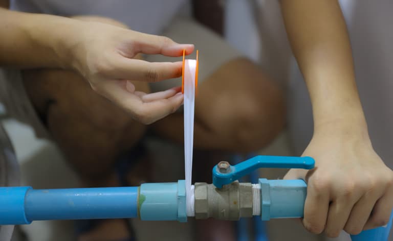 Hands applying thread-seal tape at a plastic pipe connection.