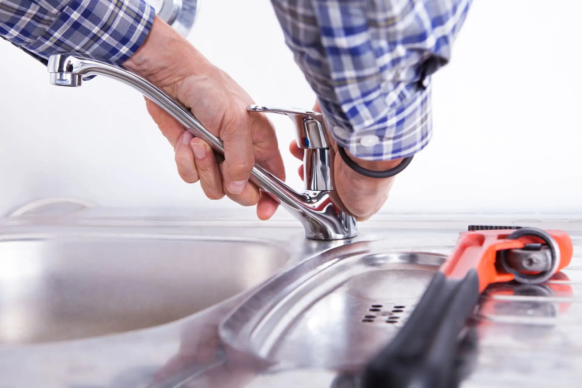 Hands adjusting a kitchen faucet beside a stainless-steel sink.
