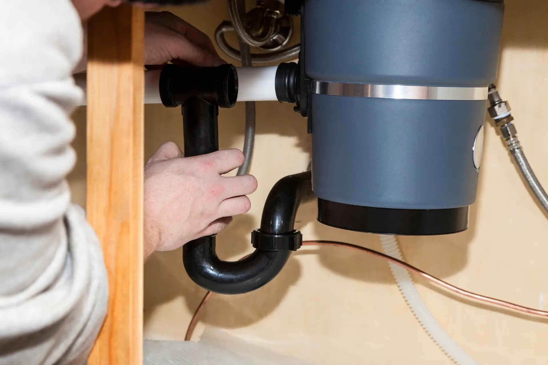 Hands working on the drain connection beside a garbage disposal.