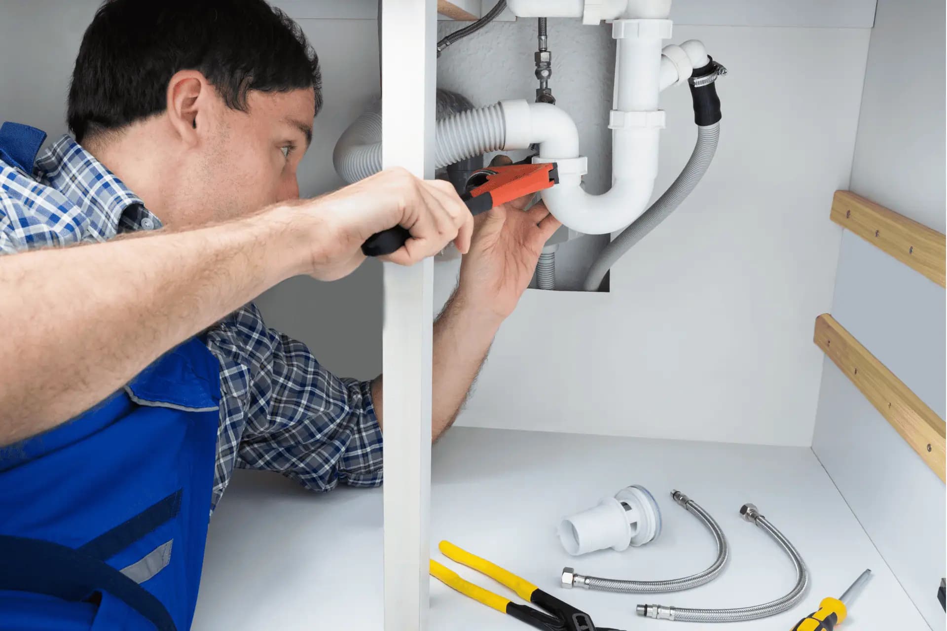 A plumber adjusting the drain fittings beneath a sink.