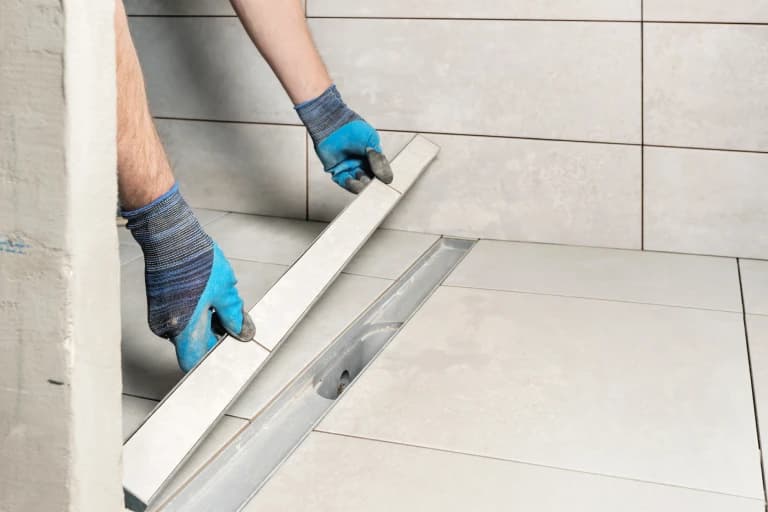 Blue-gloved hands fitting a tile-in shower drain cover.