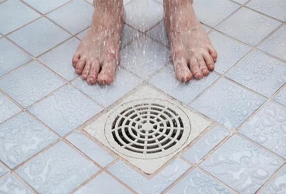 Close up of feet standing next to a shower drain