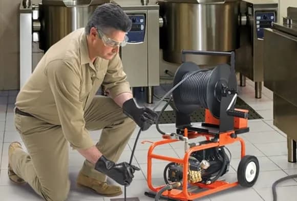 A plumber using a hydro-jetting machine on a floor drain