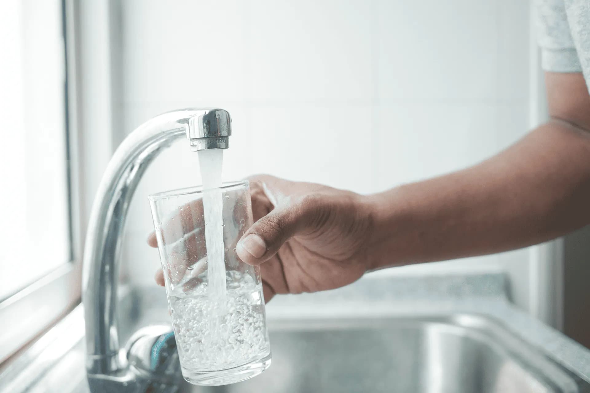 a person fills a glass of water using a touchless faucet