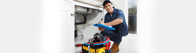 Friendly plumber hunkered beside a kitchen drain with drain cleaning equipment